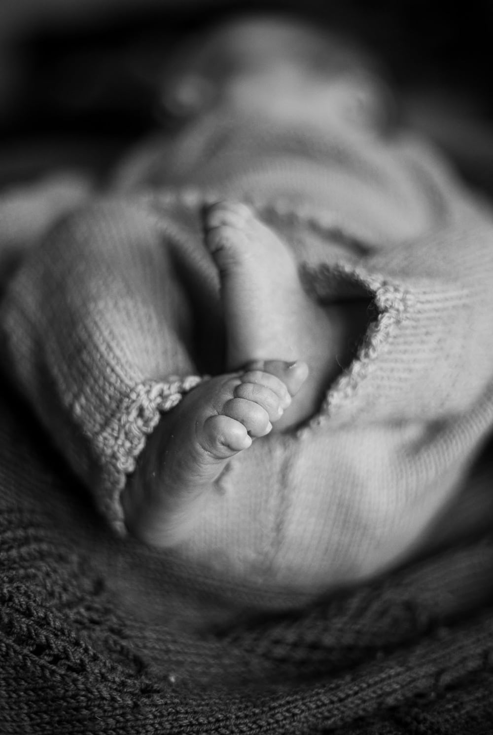 Babyfødder der kigger frem fra en strikket dragt i sort-hvid. Stemningsfuld babyfotografering for mødregrupper i Randers.