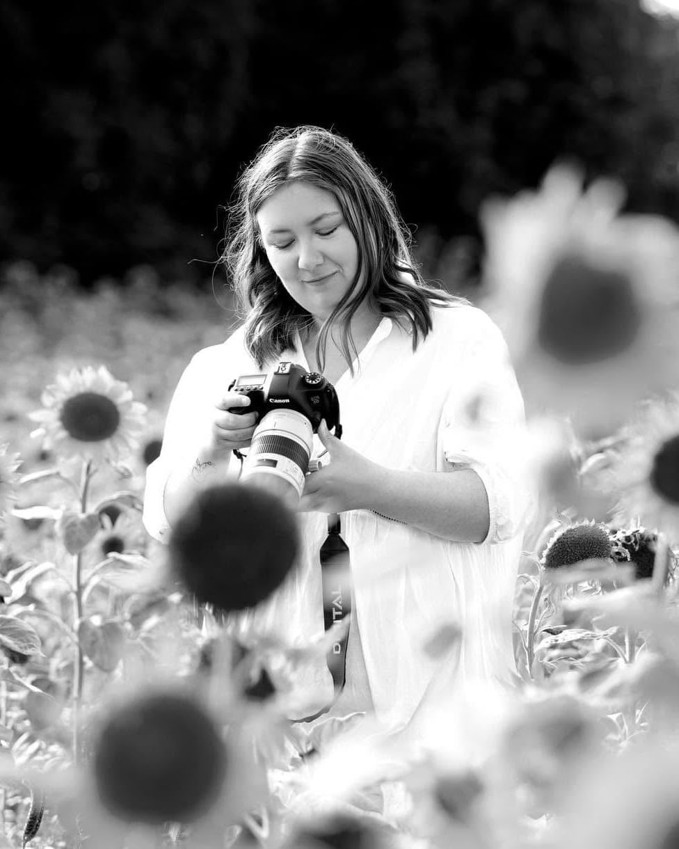 Fotograf Emma Elise med sit kamera i en solsikkemark – naturlig bryllups-, familie- og konfirmationsfotografering i Randers, Østjylland og Jylland